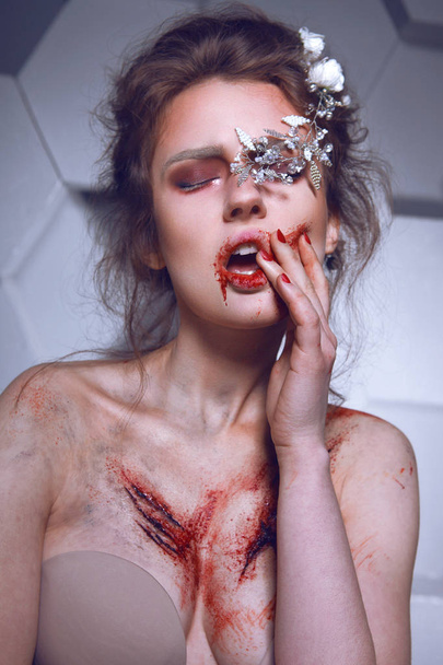 Brunette with white flowers in her hairstyle and with bloody scars on her chest on grey background - Foto, imagen
