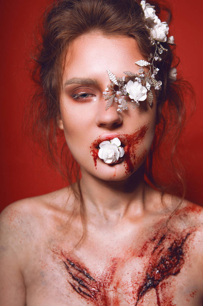 Brunette with white flowers in her hairstyle and with bloody scars on her chest on red background - Valokuva, kuva
