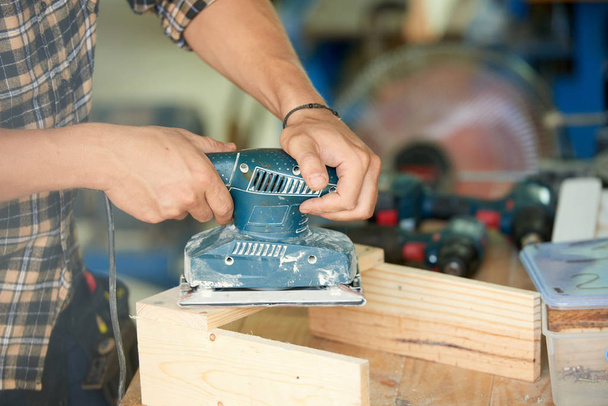Close-up image of carpenter polishing wooden plank with sanding machine - Photo, Image
