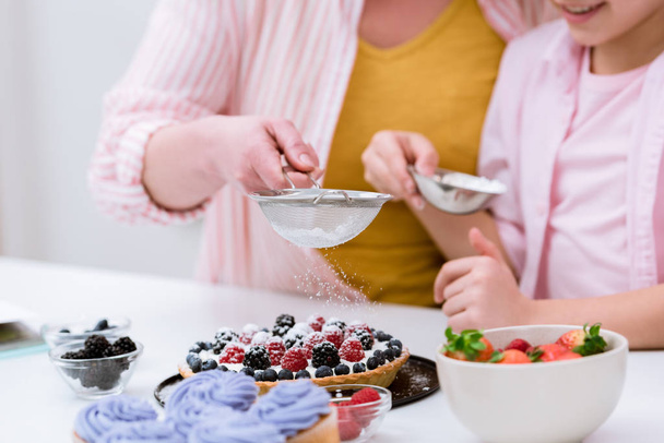 cropped shot of grandmother and little granddaughter pouring sugar powder onto tart with berries - Valokuva, kuva