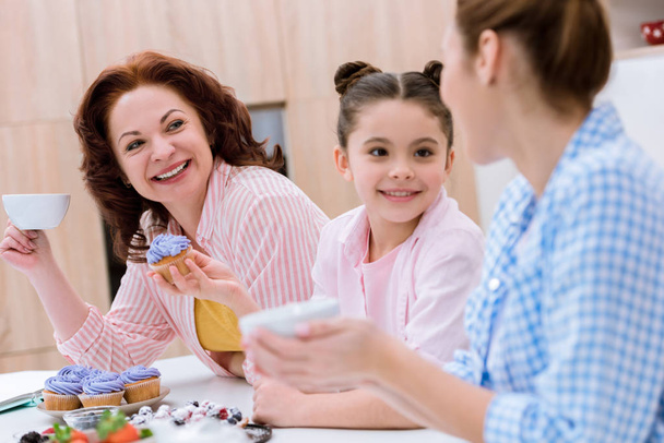 trois générations de femmes passent du temps ensemble sur la cuisine et manger des desserts avec du thé à la cuisine
 - Photo, image