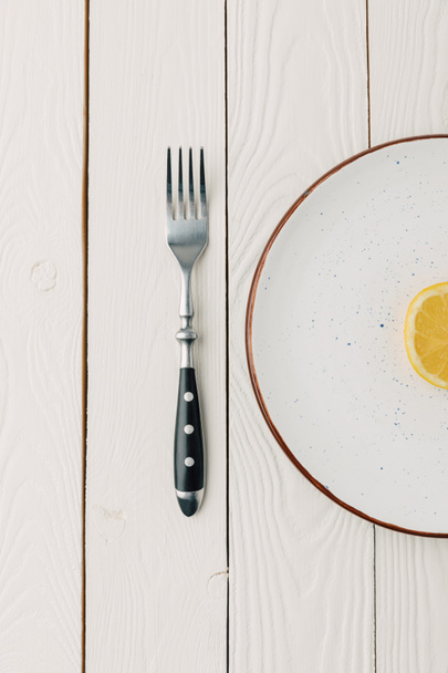 Half of juicy lemon on plate with fork on white wooden background - Photo, Image