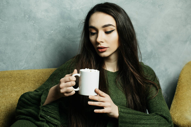 Beautiful and cute. Beautiful young woman holding coffee cup and  sitting on chair at home. Lifestyle concept. - 写真・画像