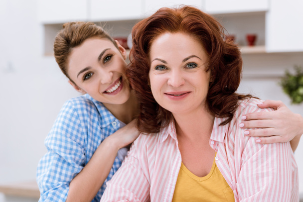 close-up portrait of young woman and her mother at kitchen looking at camera - Foto, Bild