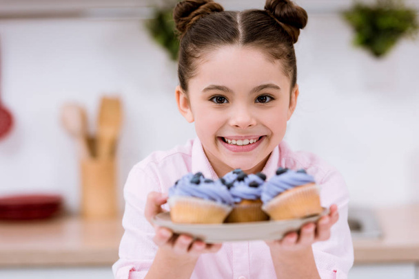 adorable little child holding plate with blueberry cupcakes - Fotó, kép