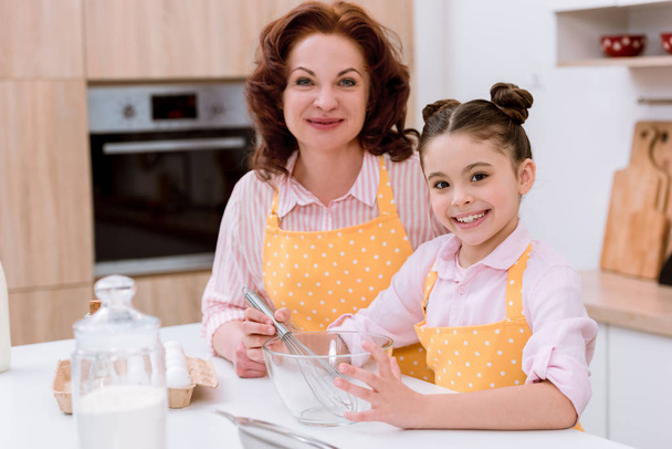happy grandmother with little granddaughter cooking together and looking at camera - Фото, зображення