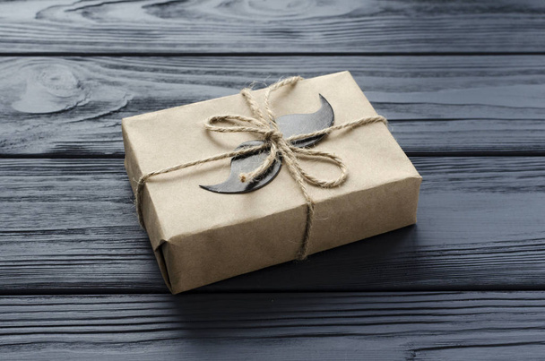 gift box wrapped in kraft paper with paper mustache on grey wood - Foto, Imagem