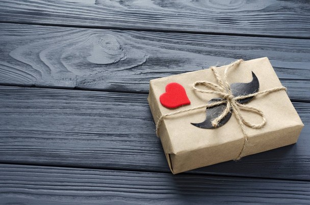 подарочная коробка, завернутая в крафт-бумагу с бумажными усами и красным слухом
 - Фото, изображение