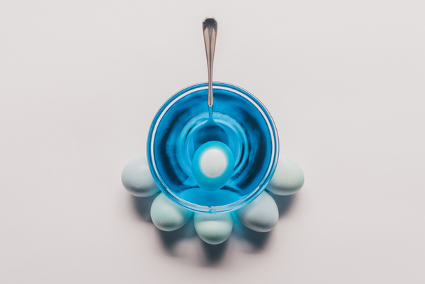 верхний вид яйца в стекле с голубой краской и куриные яйца на белой поверхности, Пасхальная концепция
 - Фото, изображение