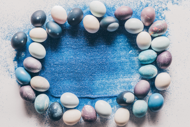 top view of painted easter eggs and blue sand on white surface - Φωτογραφία, εικόνα