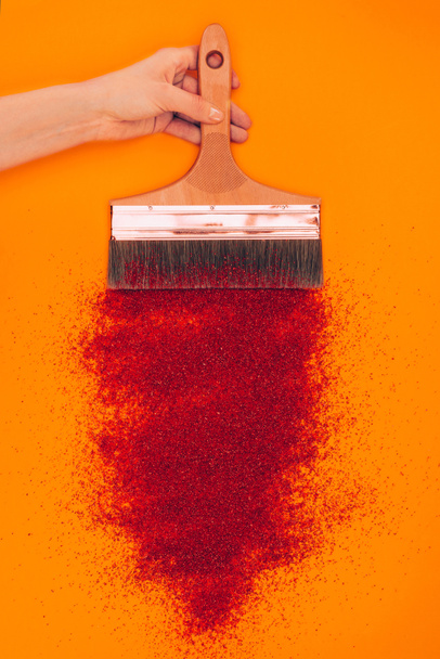 cropped image of woman holding brush above red sand isolated on orange - Foto, Imagen