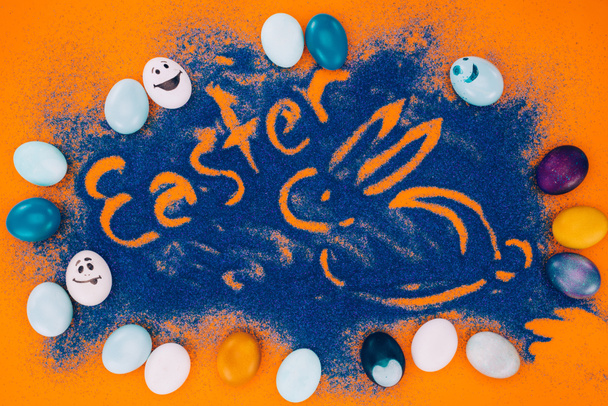 top view of easter sign with rabbit made of blue sand with chicken eggs on orange - 写真・画像