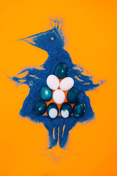 vue du dessus du poulet de Pâques bleu fait de sable avec des œufs peints isolés sur orange
  - Photo, image