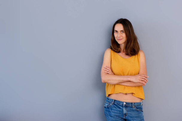 Portrait of confident older woman standing by gray wall with arms crossed - Photo, Image