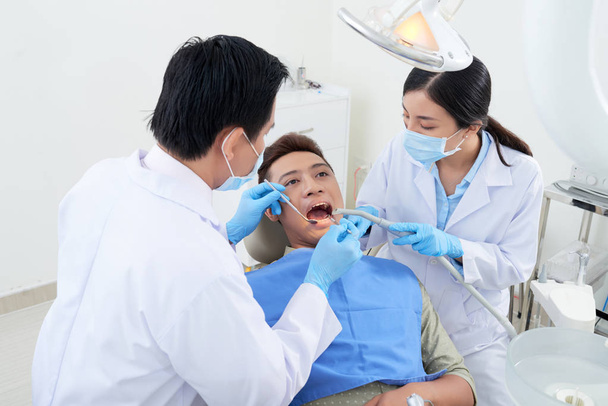 Dentist and nurse using mouth mirror, suction tube and dental explorer when examining teeth of patient - Photo, Image