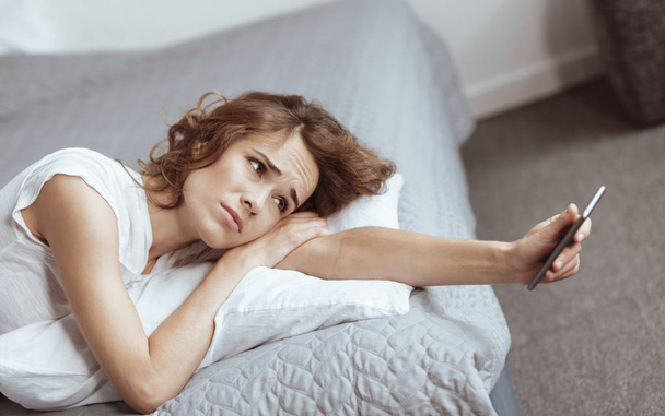 Femme déprimée couchée sur le lit et regardant smartphone
 - Photo, image