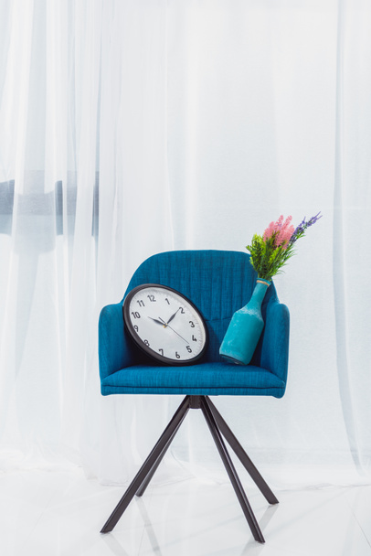 Jarrón y reloj en silla moderna azul en la habitación delante de la ventana
 - Foto, imagen