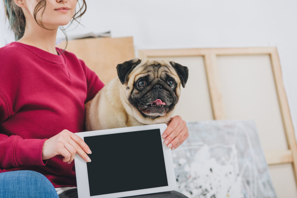 Young woman showing tablet screen and hugging pug dog - Foto, imagen