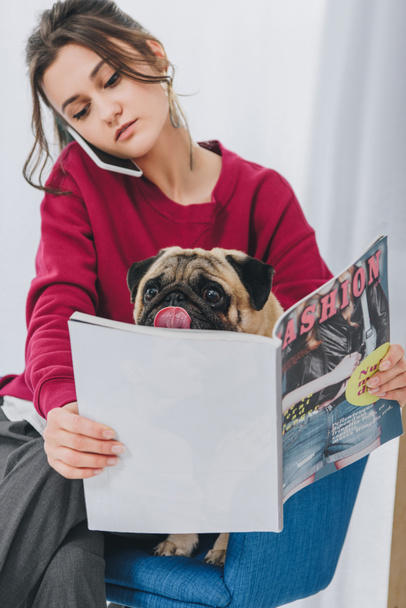 Attractive young girl talking on the phone and hugging pug dog - Zdjęcie, obraz