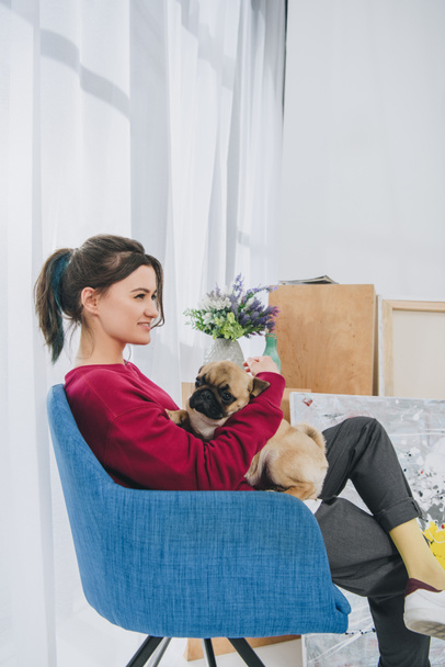 Young girl cuddling pug in chair in modern room - Fotoğraf, Görsel