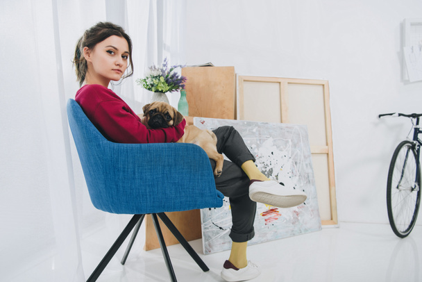 Ładna pani przytulanie Mops w fotelu w nowoczesnym pokoju - Zdjęcie, obraz
