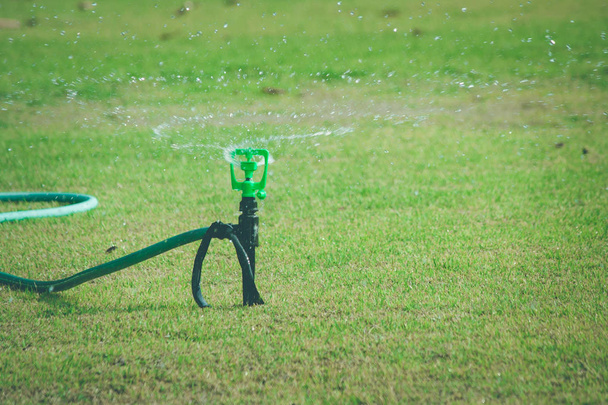 Lawn víz sprinkler a zöld fű permetezés és öntözés rét a szabadtéri kertben nyáron szezonális. (Szelektív fókusz) - Fotó, kép