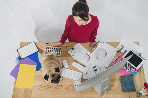 Young woman working with sketches with cute pug on working table with computer - Photo, Image