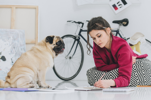 Attractive young girl drawing on floor with pug pet - Foto, immagini