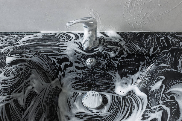 Black glass sink  in soap foam. Cleaning the sink.  - Photo, Image