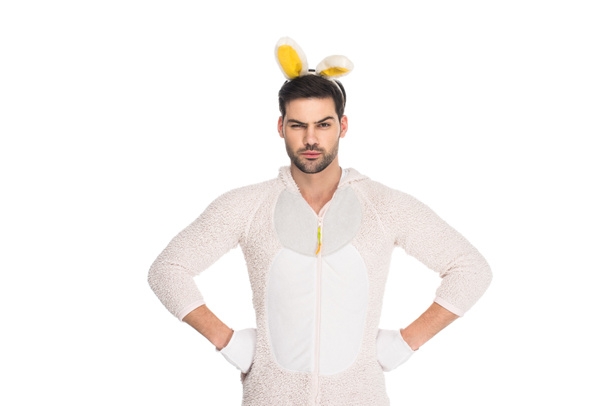 Uomo in costume da coniglio che chiude un occhio e tiene le braccia sulle cosce isolate su bianco, concetto pasquale
 - Foto, immagini