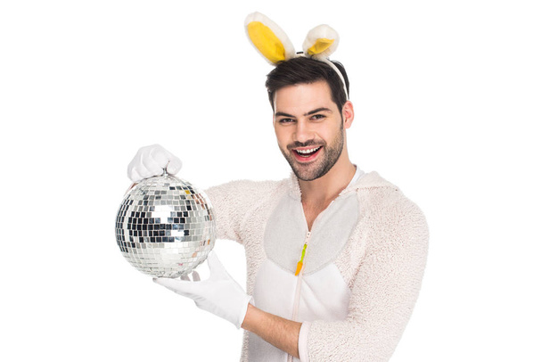 Улыбающийся человек в костюме кролика держит диско-шар изолированный на белой, пасхальной концепции
 - Фото, изображение