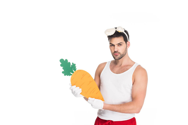 Junger Mann mit Hasenohren hält große Karotte auf weißem, Osterkonzept - Foto, Bild