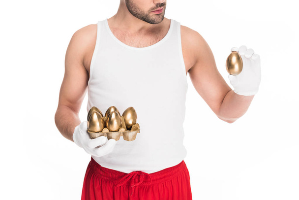 Bijgesneden afbeelding van een jonge man die gouden eieren geïsoleerd op wit, Pasen concept - Foto, afbeelding