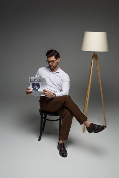 Young businessman sitting on chair and reading newspaper on grey - Фото, зображення
