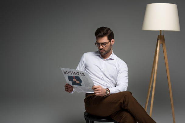  stylish businessman reading newspaper near floor lamp isolated on grey - Photo, Image