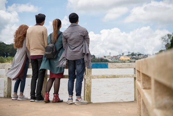 Rear view of young people enjoying the view of the river and city from the bridge - Foto, imagen