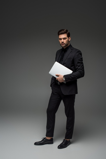stylish businessman standing with laptop on grey - Zdjęcie, obraz