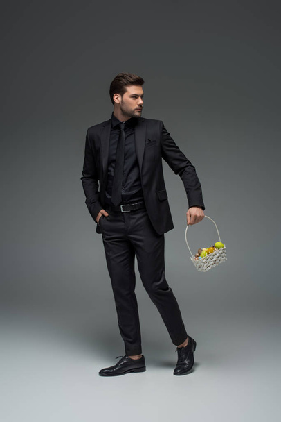 Young businessman carrying basket of fruits on grey - Fotoğraf, Görsel