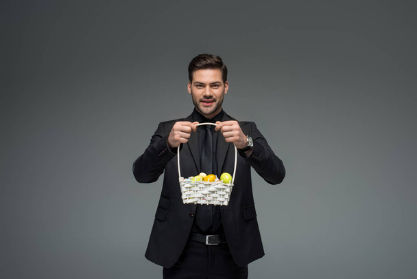 Lachende zakenman holding mand met fruit geïsoleerd op grijs - Foto, afbeelding