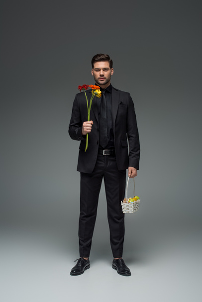 Stylish businessman holding flowers and basket with fruits on grey, international womens day concept - 写真・画像