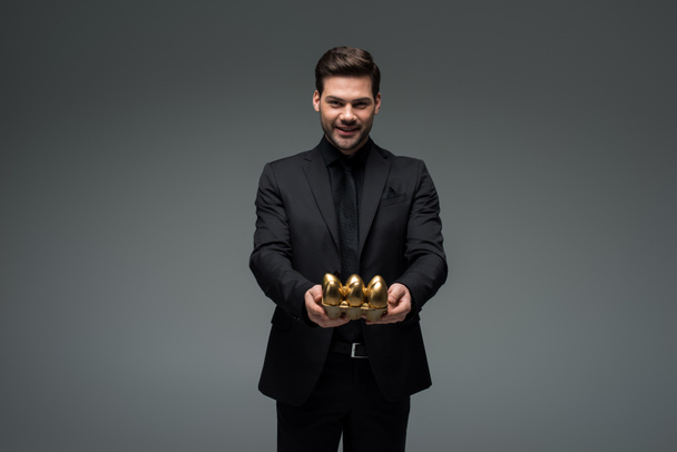 Smiling man with golden eggs isolated on grey, easter concept - Fotografie, Obrázek