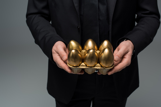 Vértes nézet of arany tojás, kezében a férfi elszigetelt a szürke, húsvéti koncepció - Fotó, kép