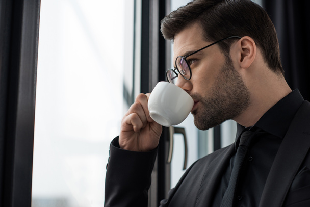 Side view of businessman in glasses drinking coffee  - 写真・画像