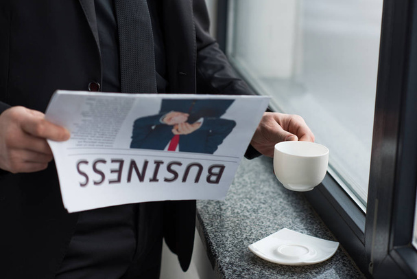Częściowy widok biznesmen czytanie gazety i trzymając kubek kawy - Zdjęcie, obraz