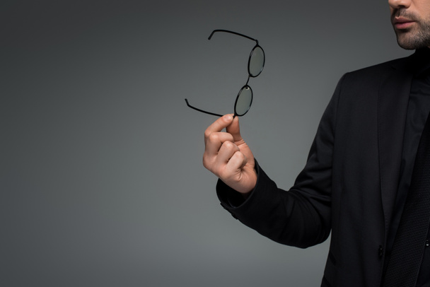 Частковий вигляд стильного чоловіка, що тримає окуляри ізольовані на сірому
 - Фото, зображення