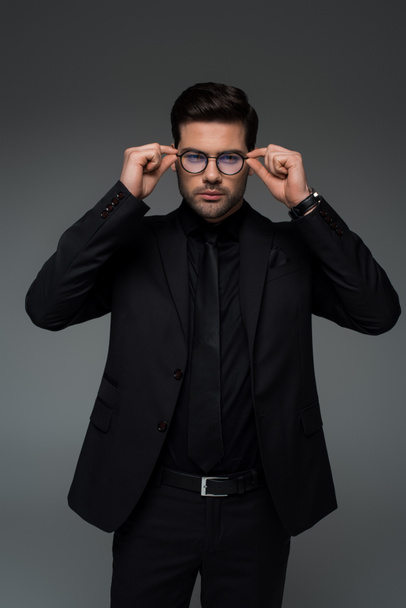 Man in stylish black suit taking off glasses isolated on grey  - Foto, afbeelding