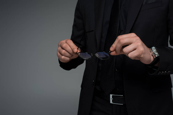 Vista parcial de las manos masculinas sosteniendo gafas aisladas en gris
 - Foto, Imagen