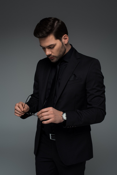 Stylish man in black suit holding glasses isolated on grey - Fotoğraf, Görsel