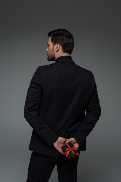 Rear view of stylish man holding gift box isolated on grey, international womens day concept - 写真・画像