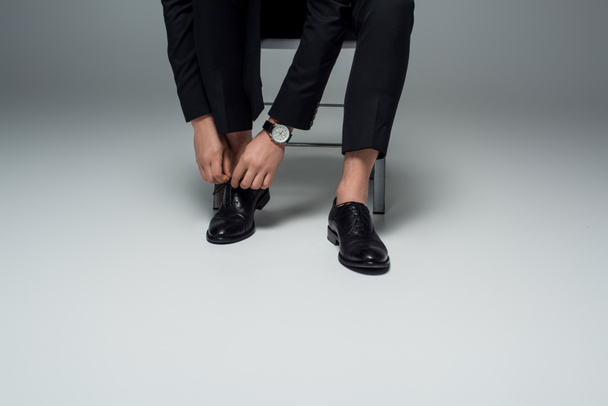 Partial view of stylish man tying shoelaces on grey - Valokuva, kuva